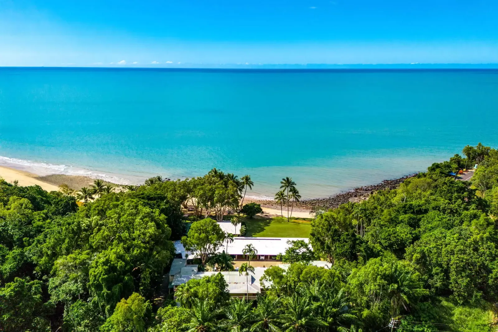 Wide aerial view of the beach, Coral Sea and resort among the trees