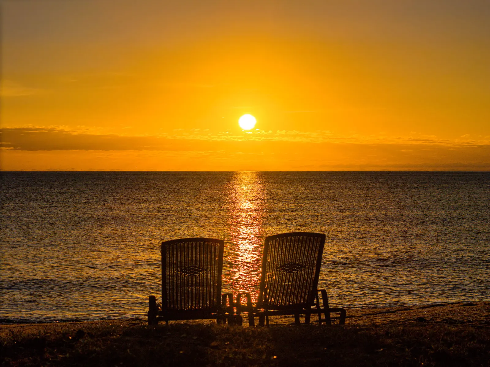 Two chairs on the sand facing the sunrise